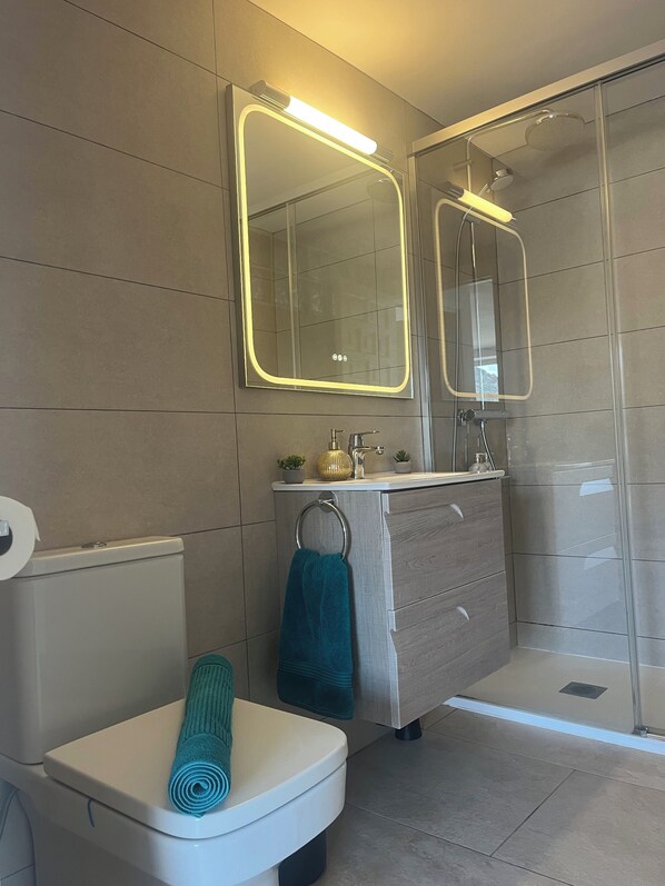 Une salle de bain moderne équipée de toilettes, d’un lavabo avec miroir et d’une douche.