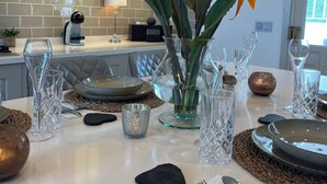 A dining area with a white table set for a meal, featuring clear glassware, a vase with a plant, and a modern pendant light.