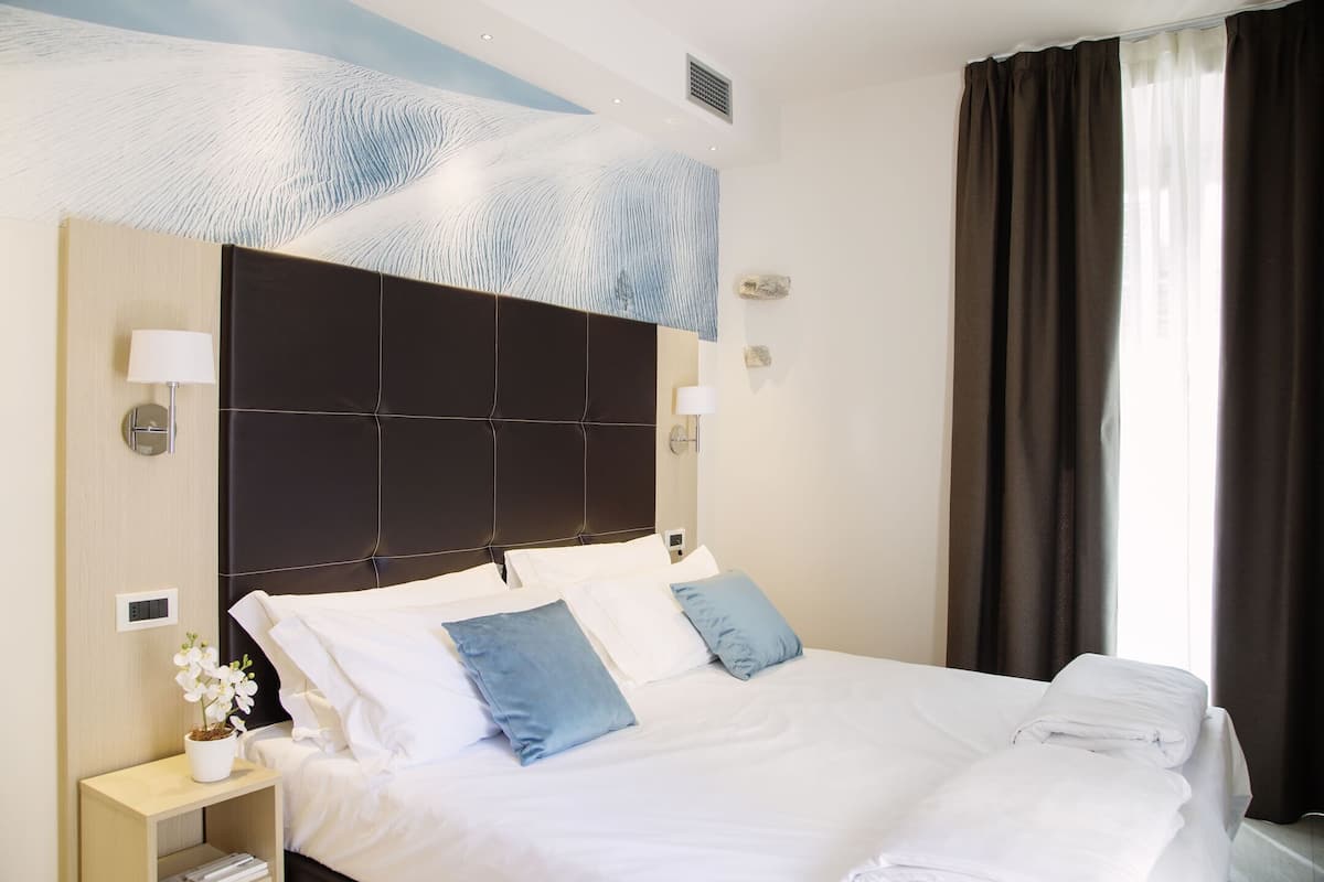 A hotel room with a large bed, two bedside lamps, a nightstand with a lamp and a small potted plant, and a ceiling with a textured design.