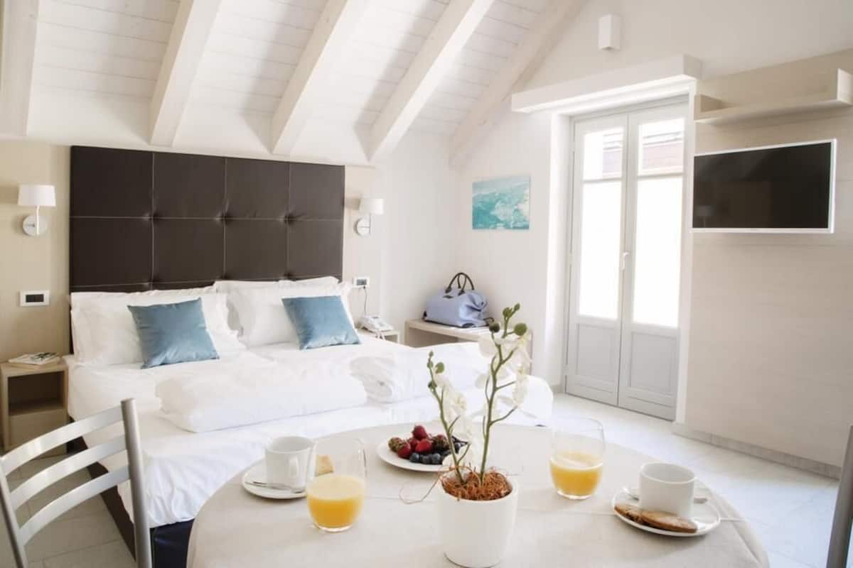 A hotel room with a bed, bedside table, and a dining table set with breakfast.