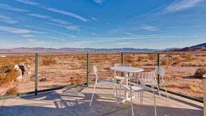 Eine Terrasse im Freien mit Tisch und Stühlen, einem Metallzaun und Blick auf eine Wüstenlandschaft.