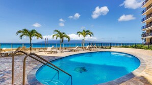 Ein Poolbereich mit Liegestühlen und Palmen, mit Blick auf einen Strand und das Meer.