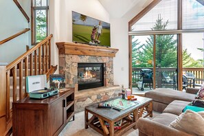A spacious living room with a stone fireplace, a large TV, and a cozy seating area with a view of the outdoors.