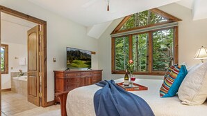 Ein Schlafzimmer mit einem großen Bett, einem Fernseher, einem Fenster mit Blick auf Bäume und einer Holzkommode.