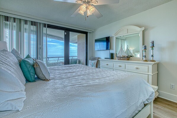 A bedroom with a large bed, a dresser, a mirror, and a view of the ocean through the window.