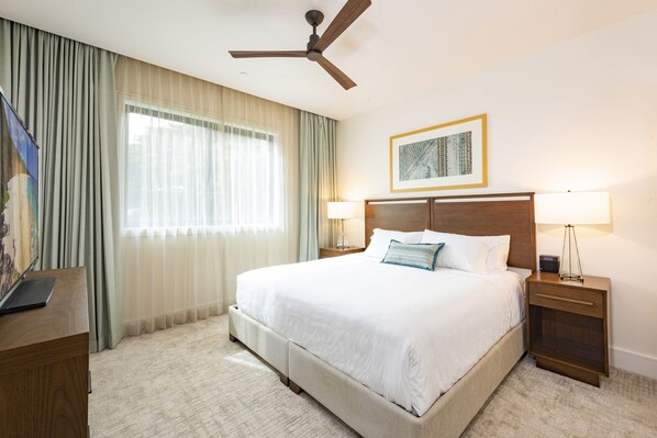 A neatly arranged hotel room with a large bed, two bedside tables, a ceiling fan, and a window with curtains.