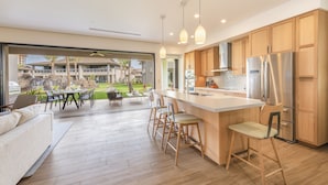 A modern kitchen with wooden cabinets, a large island with bar stools, and a view of a landscaped outdoor area.
