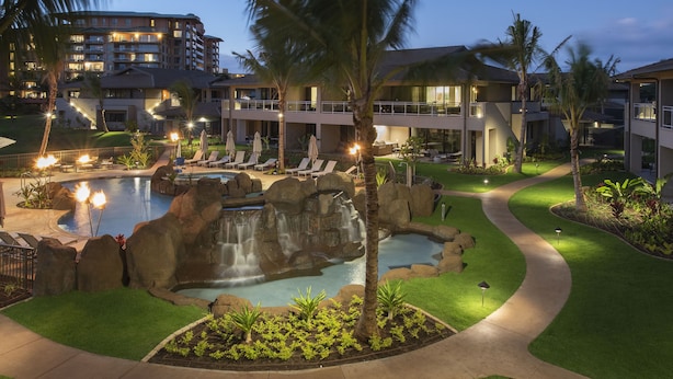 A resort pool area with a waterfall, lounge chairs, and a well-lit pathway.