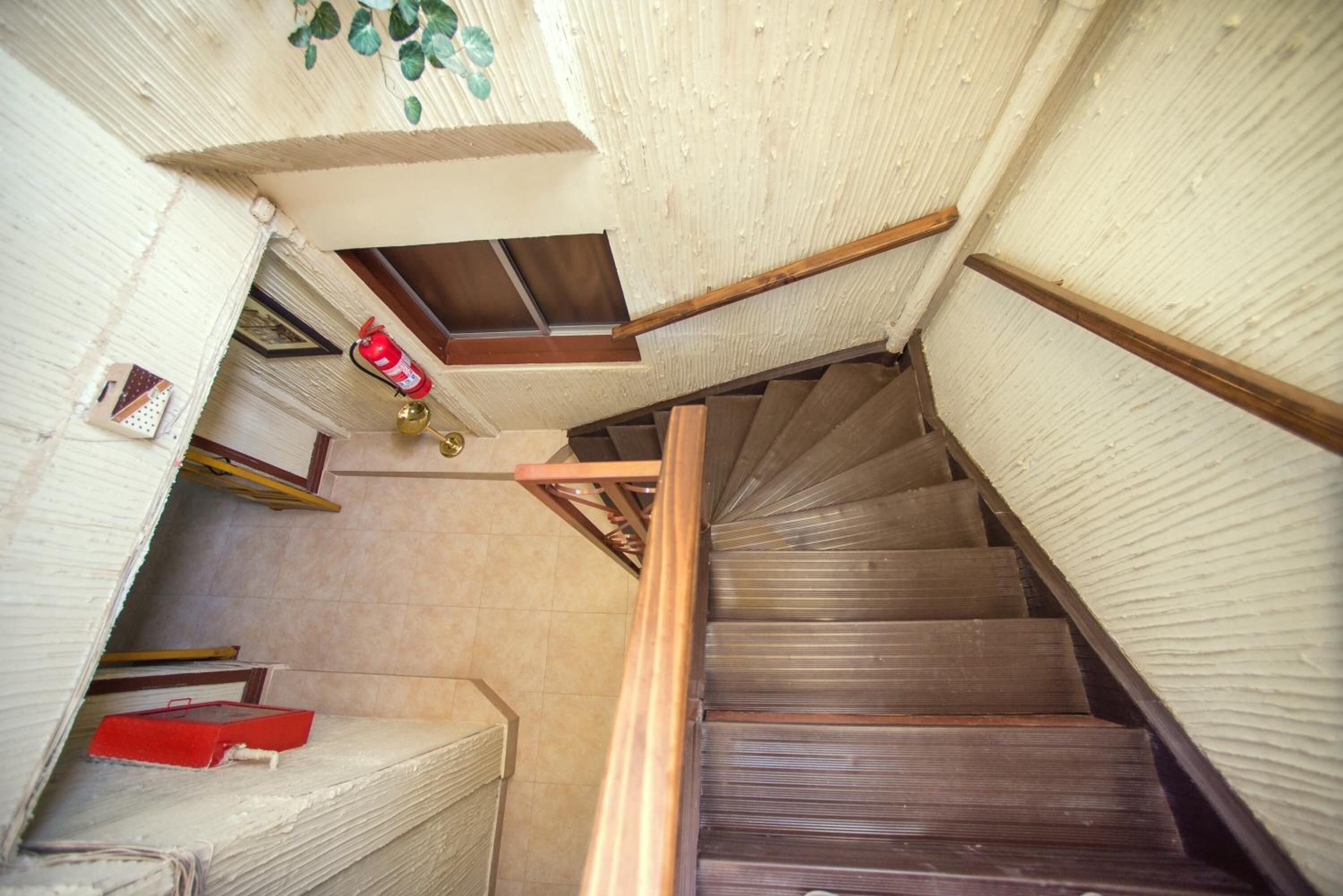 A spiral staircase with wooden steps and a handrail, leading to a landing with a small window and a fire extinguisher.