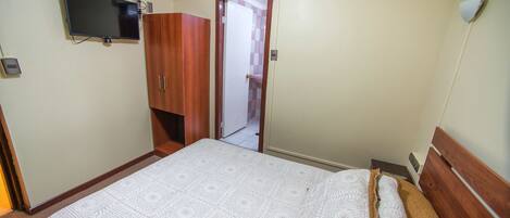A bedroom with a bed, a television mounted on the wall, and a wardrobe.