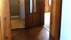 Ein heller Innenbereich mit Holzboden und -wänden, einer Tür zu einem Badezimmer, einem kleinen Spiegel und einem Thermostat an der Wand.