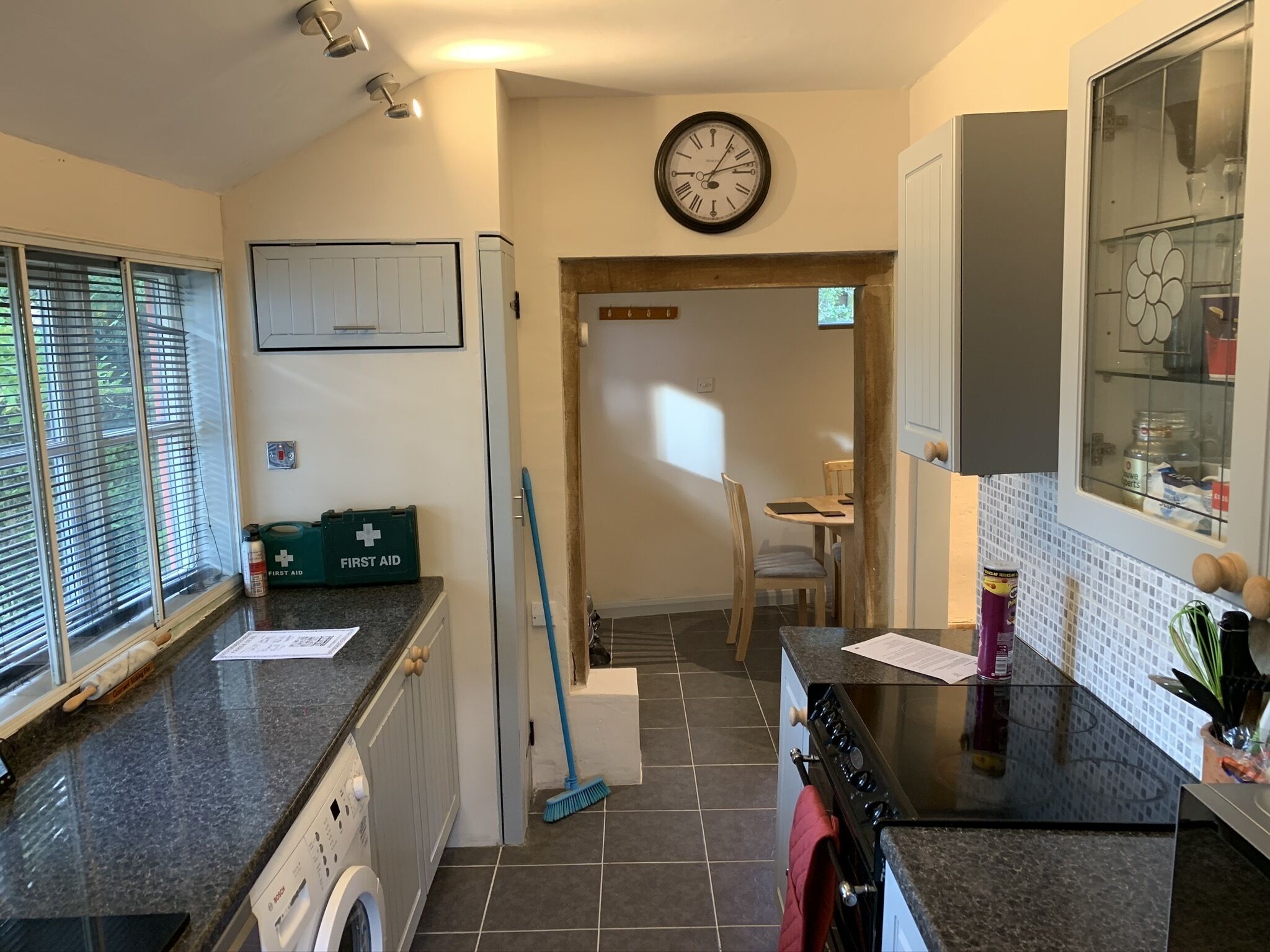 A kitchen with a washing machine, a broom, and a first aid kit.