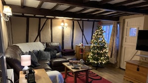 A cozy living room with a leather sofa, a wooden coffee table, a red rug, a Christmas tree, and a flat-screen TV. - Myrtle Cottage (Diss)