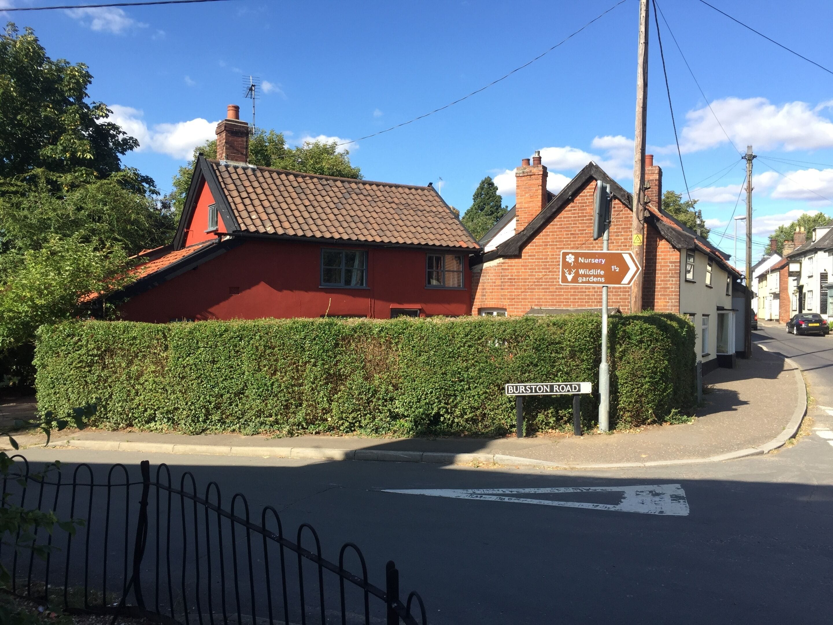 A red house with a sign indicating a nursery and wildlife gardens nearby.