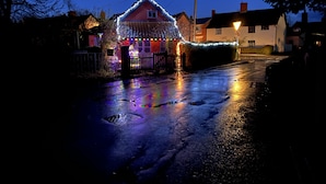 A house with a red facade and white trim, surrounded by a fence and decorated with colorful lights. - Myrtle Cottage (Diss)