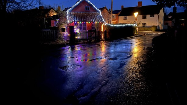 A house with a red facade and white trim, surrounded by a fence and decorated with colorful lights. - Myrtle Cottage (Diss)