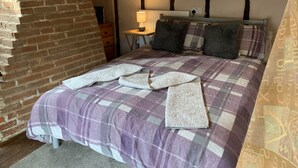A bedroom with a checkered bedspread, a brick wall, and a wooden ceiling. - Myrtle Cottage (Diss)