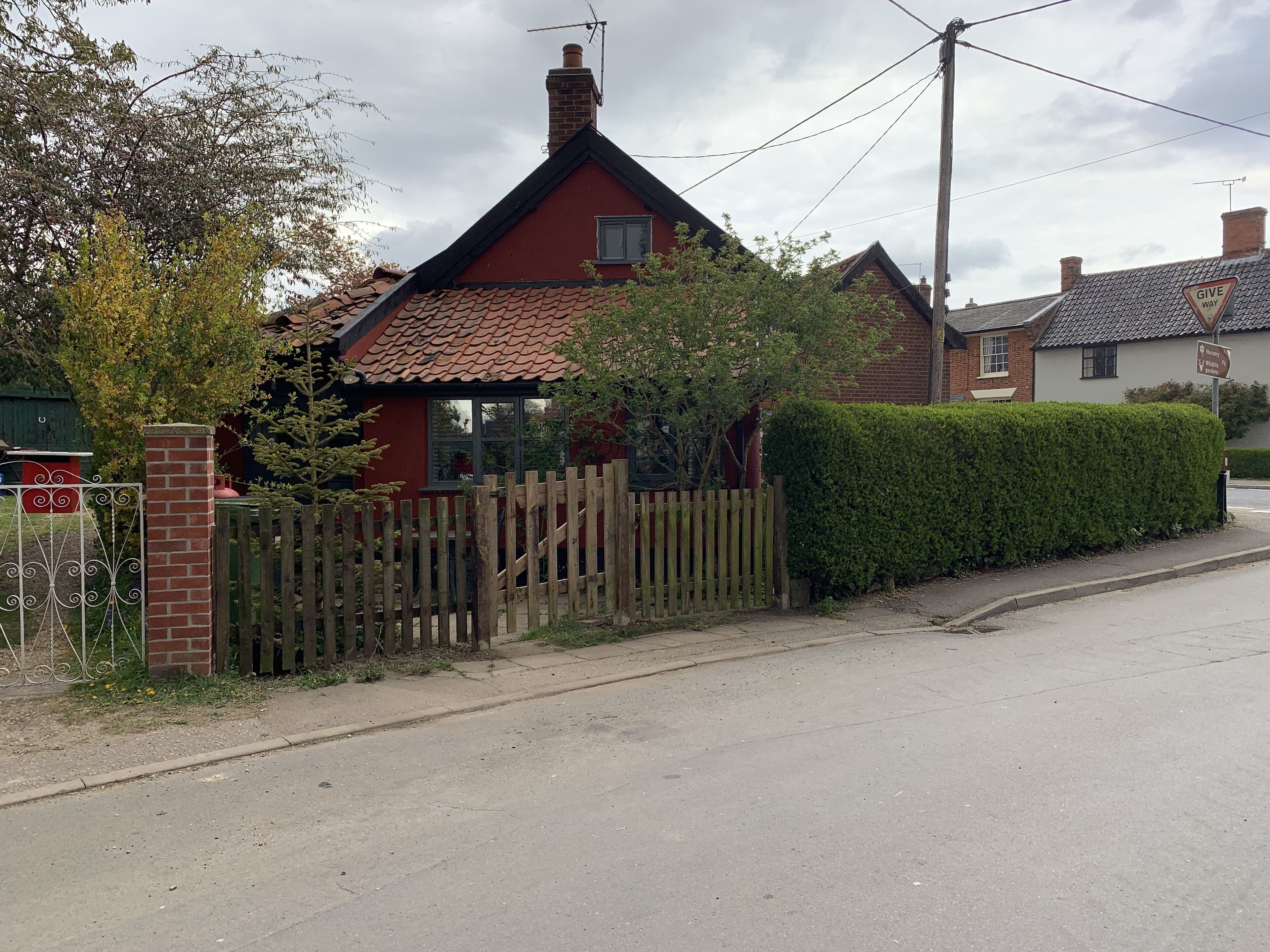 A red house with a tiled roof, a wooden fence, and a hedge along the street.