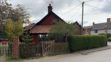 A red house with a tiled roof, a wooden fence, and a hedge along the street.
