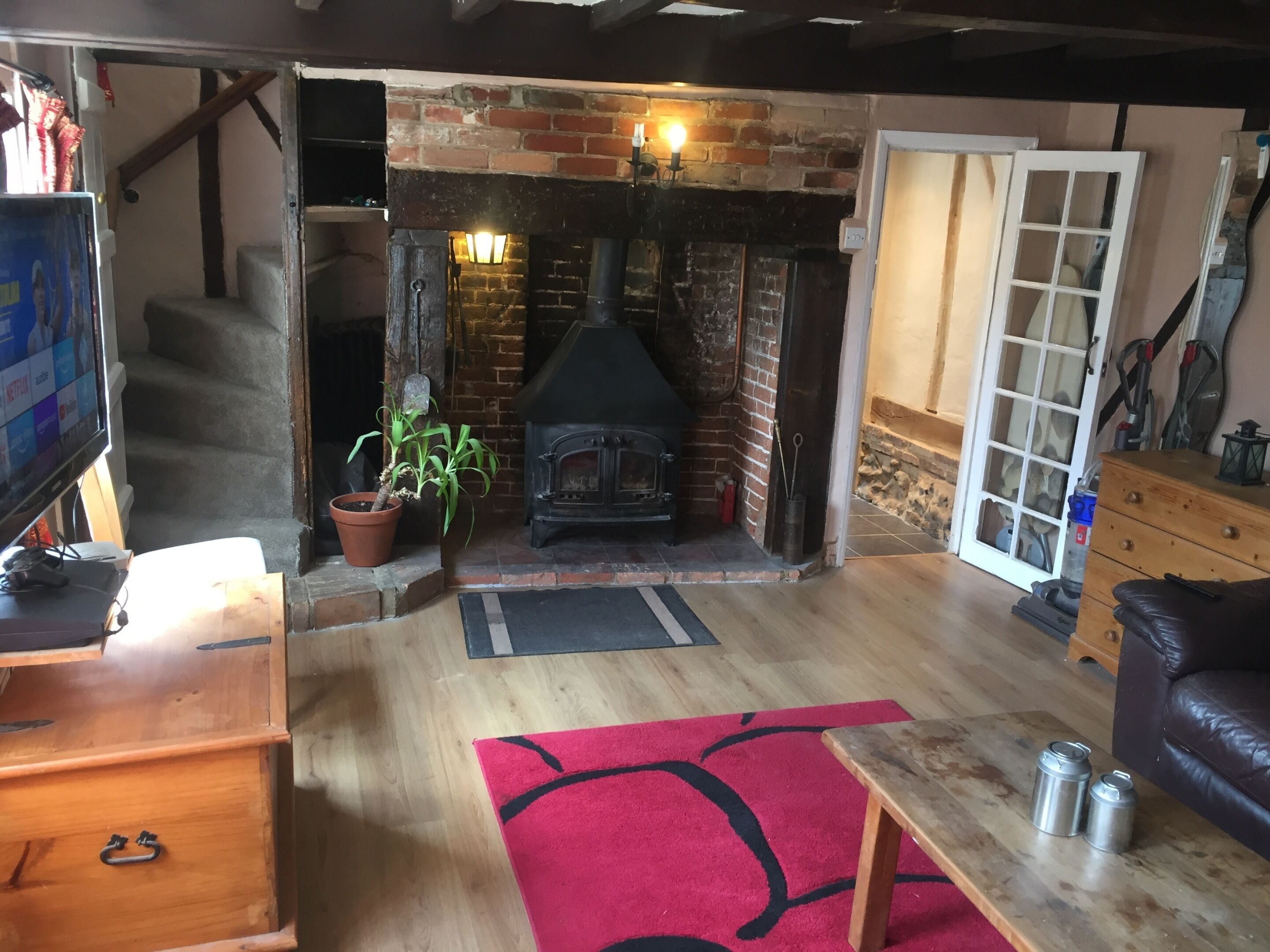 A cozy living room with a brick fireplace, wooden flooring, a red rug, a wooden coffee table, and a leather sofa.