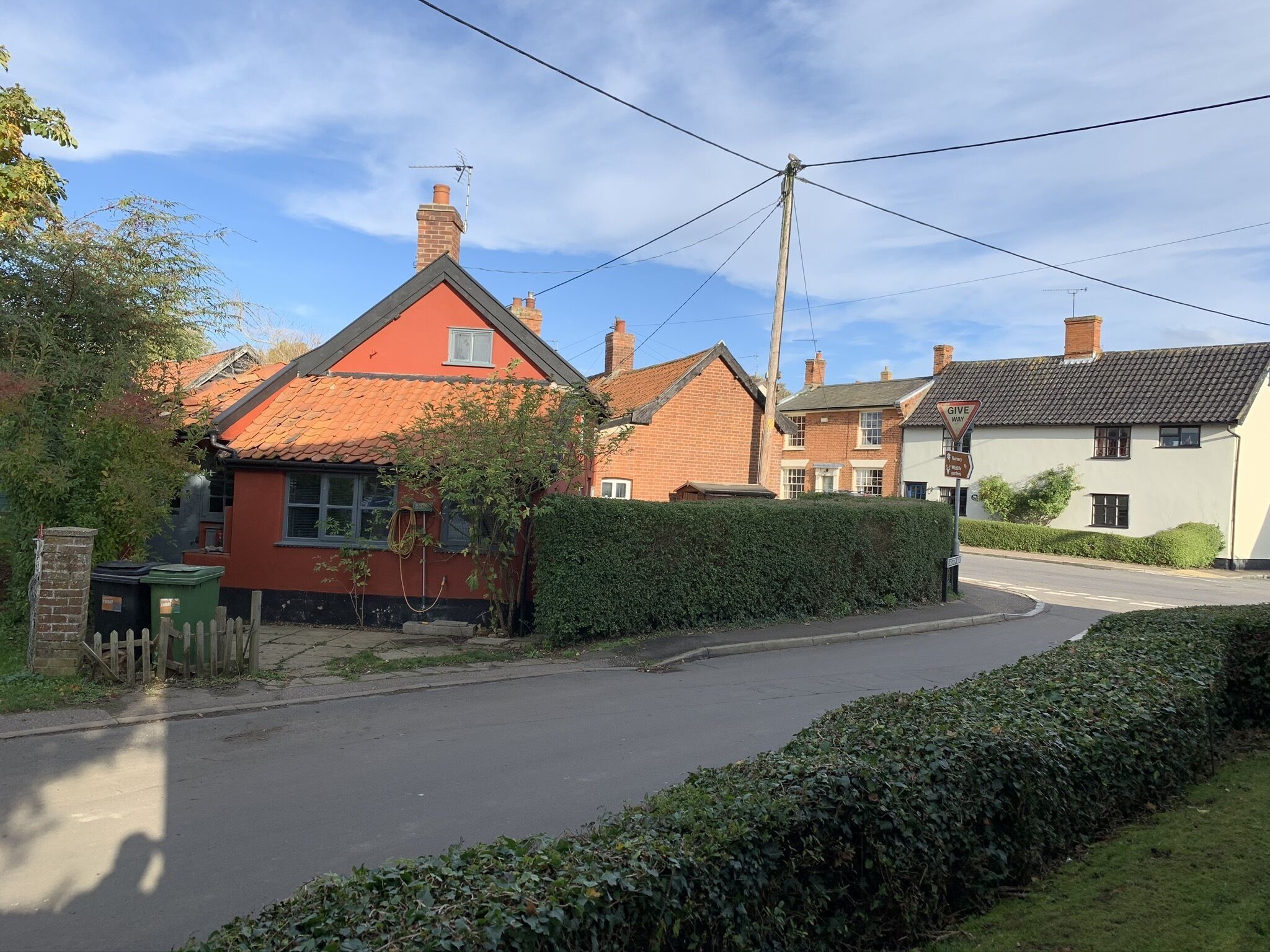 A residential street with houses, a hedge, and a clear sky.