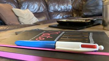 A notebook with a blue pen on a pink mat, a black object, and a metal container on a wooden table.