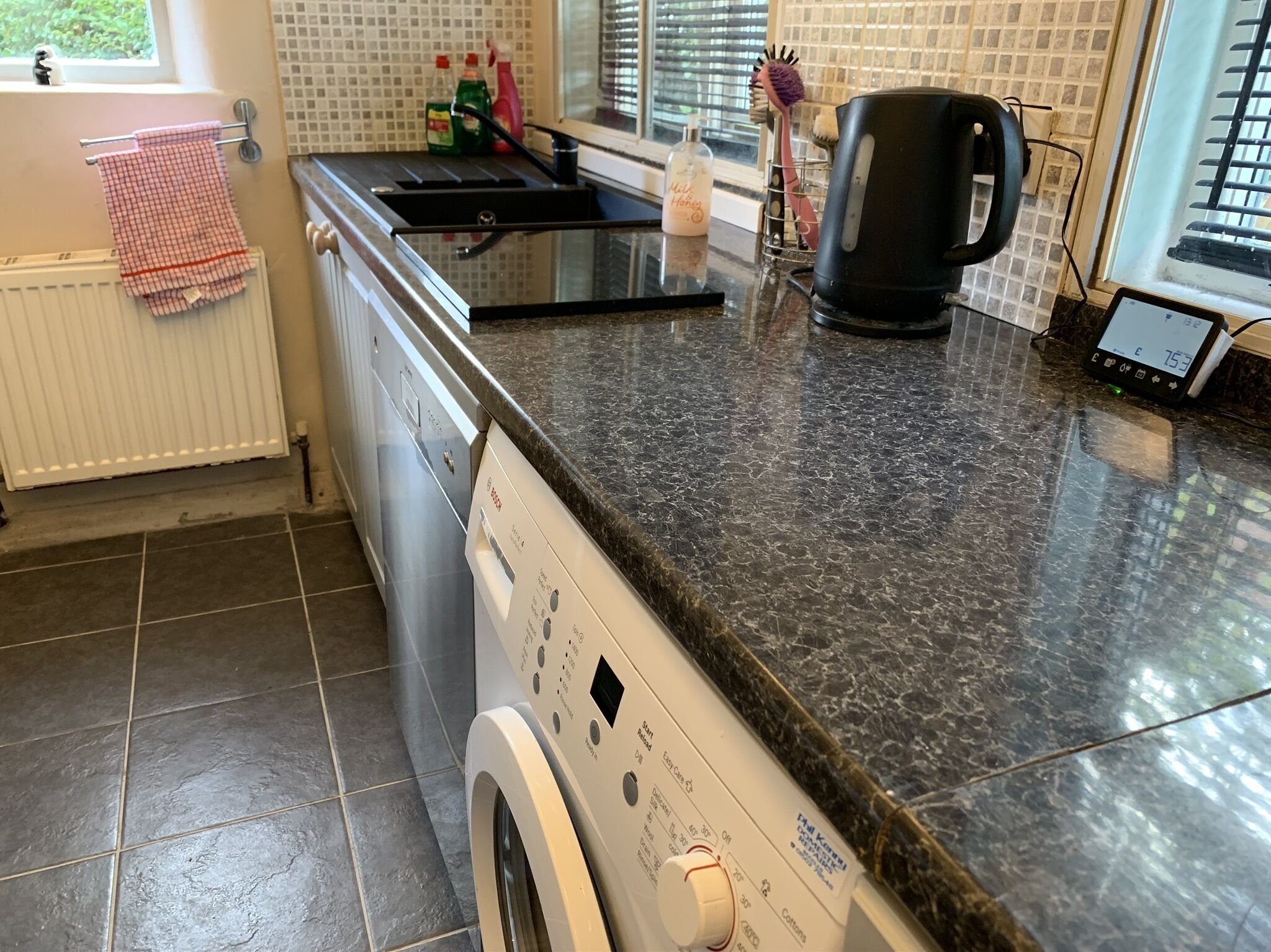 A kitchen with a washing machine, a coffee maker, and a kettle on the counter.