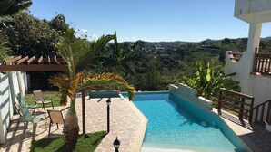 Piscina com deck revestido, cercada por vegetação e vista para uma paisagem montanhosa.