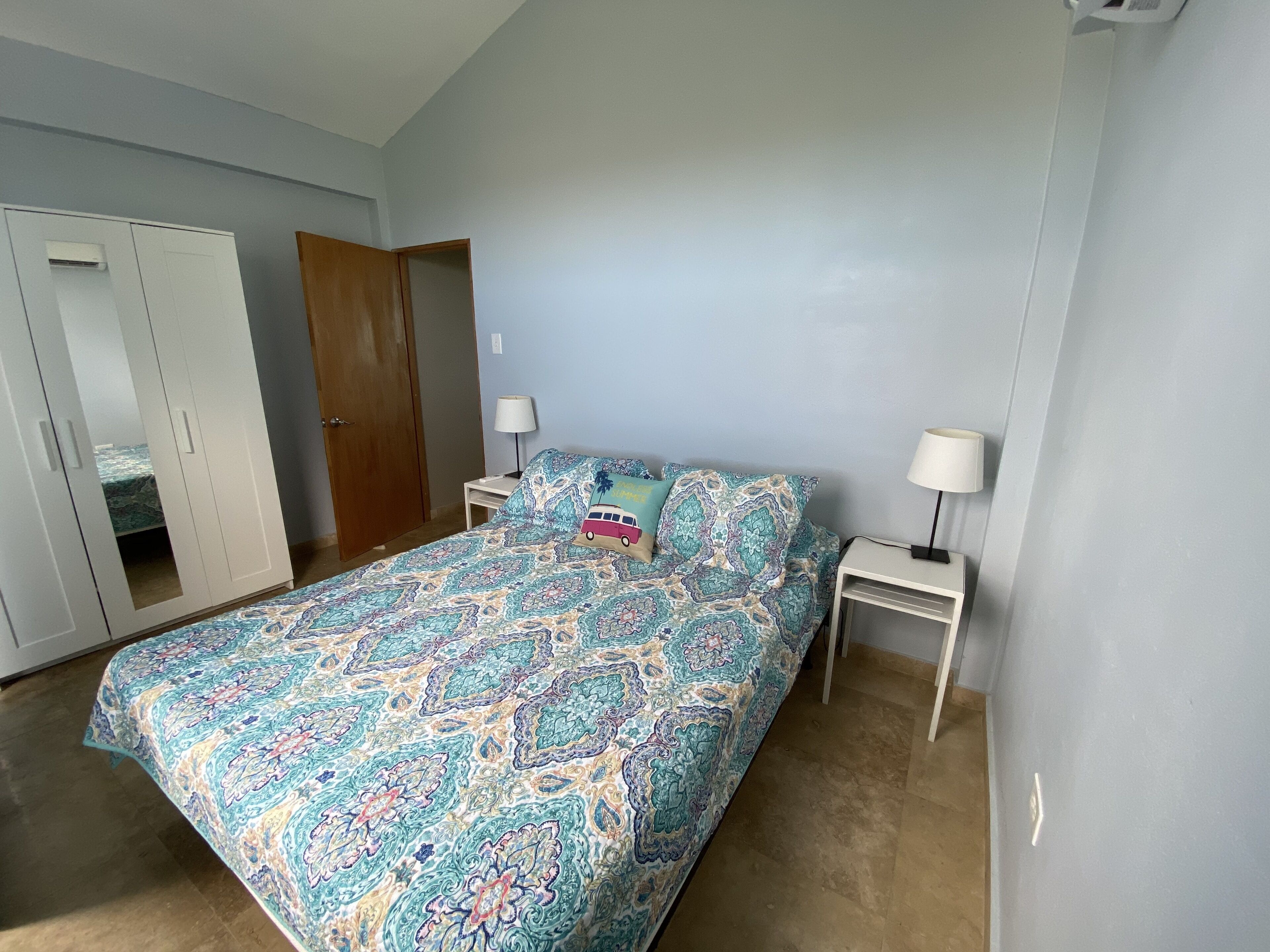 Un dormitorio con cama, dos mesitas de noche, un armario y una puerta.