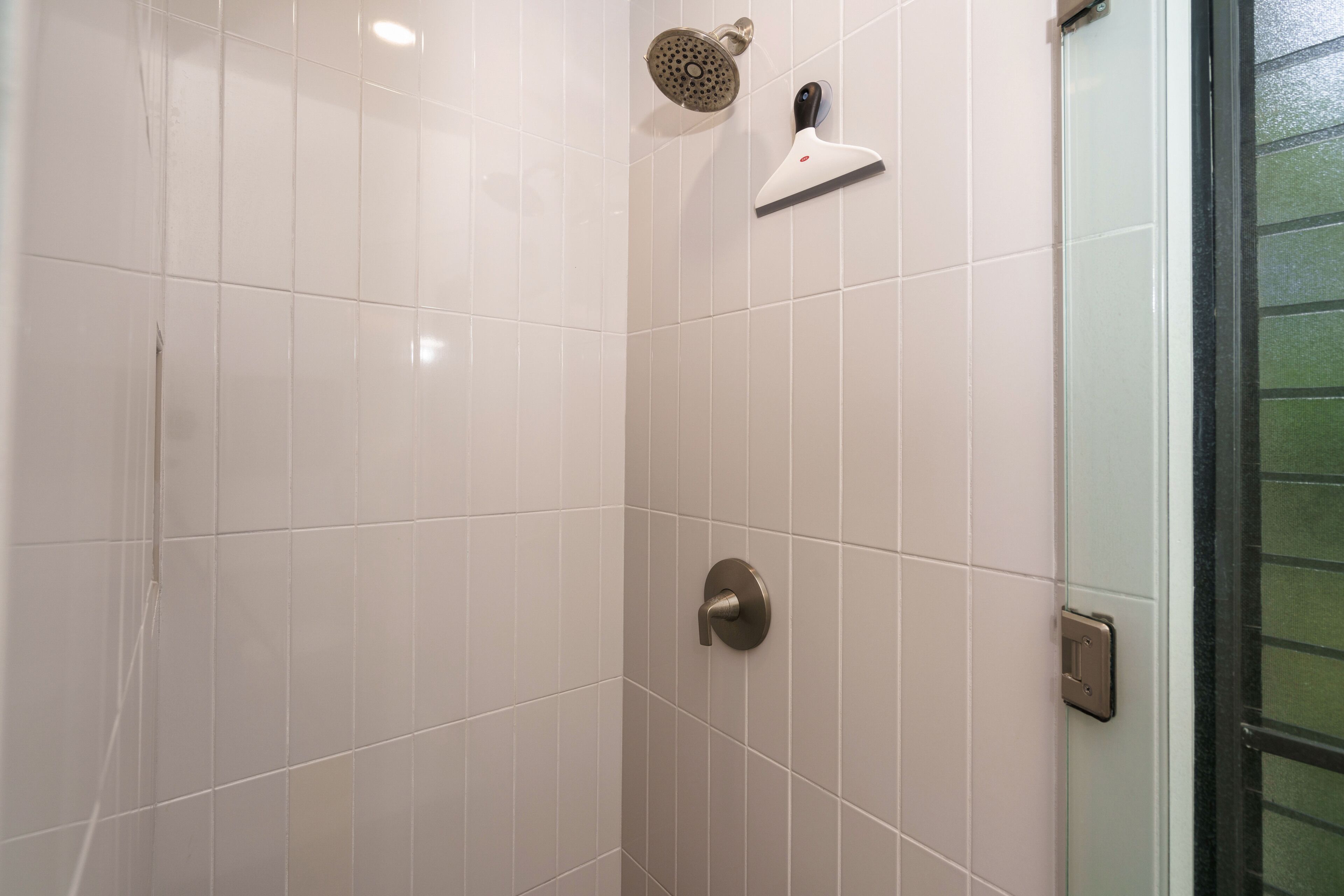 Un espace douche avec des carreaux blancs, une douchette à main et un panneau de commande fixé au mur.