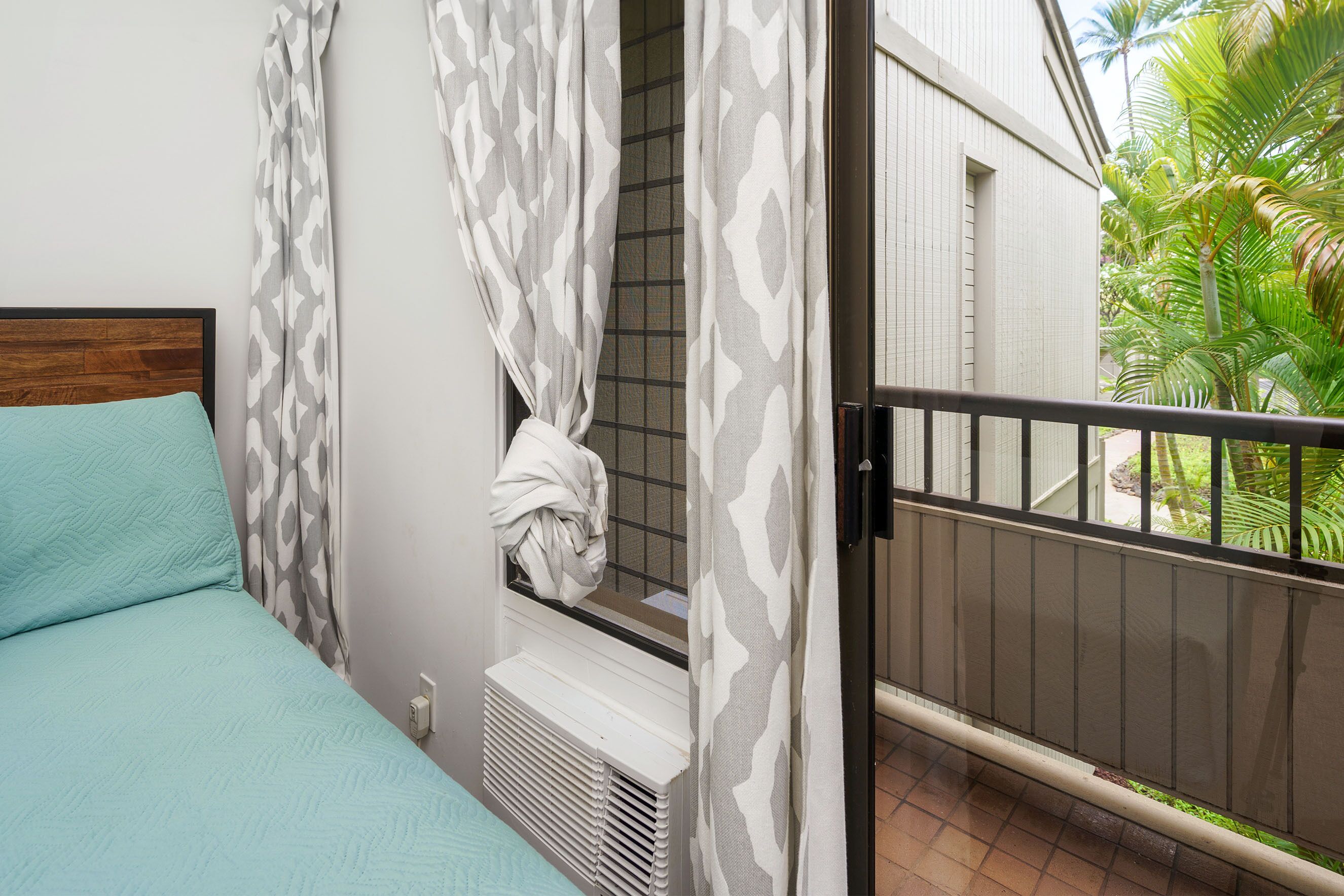 Un dormitorio con cama, ventana con cortinas, radiador y vistas a un balcón con plantas.