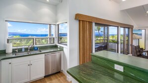 Eine moderne Küche mit Meerblick, einem großen Fenster und einer grünen Arbeitsplatte.