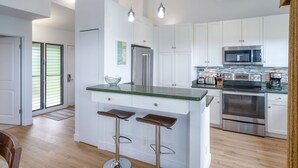 Eine moderne Küche mit weißen Schränken, Edelstahlgeräten und einer Kücheninsel mit grüner Arbeitsplatte sowie zwei Barhocker.