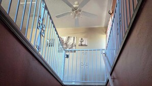 A staircase with a ceiling fan, metal railings, and a door with a number plate.