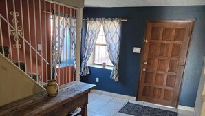 A room with a wooden bench, a tiled floor, a door, and a window with patterned curtains.