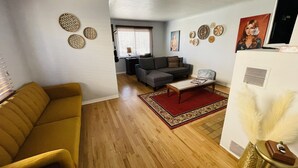 A living room with a sofa, a coffee table, and a rug. There is a TV on a stand and a window with blinds. - Gorgeous, private, comfy, clean & close to EDO (Albuquerque)