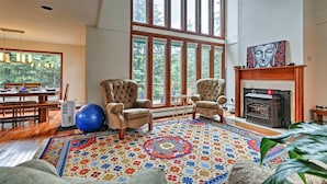 A spacious living room with a high ceiling, large windows, a fireplace, and a colorful rug.
