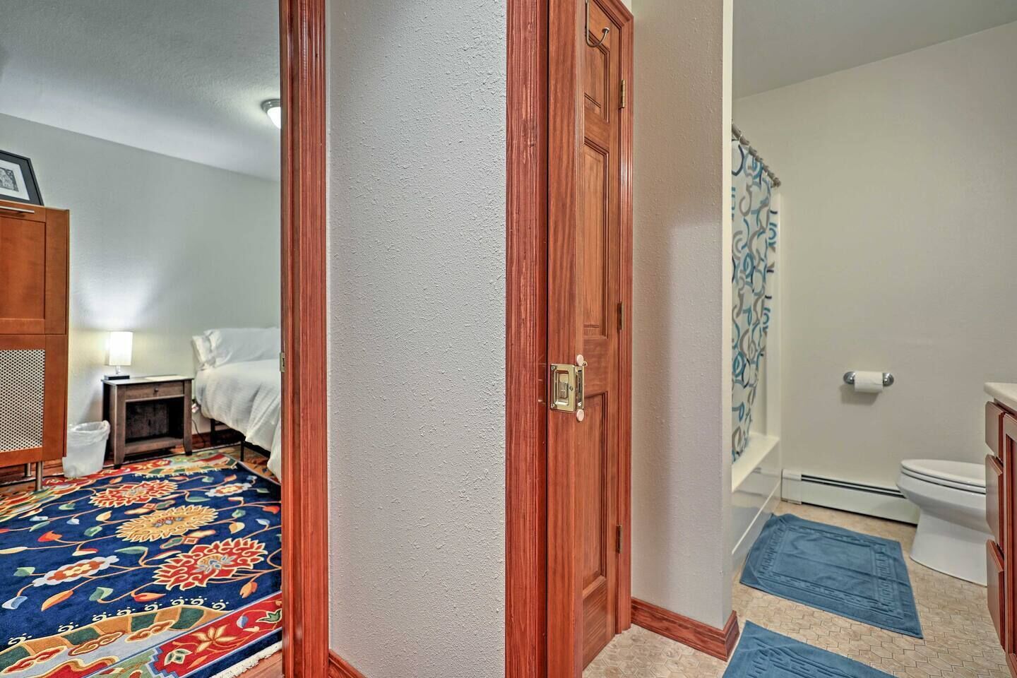 A hotel room with a bed, nightstand, and a colorful rug.