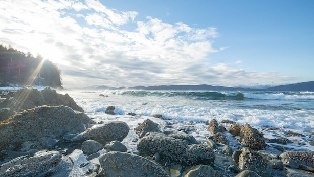 A rocky shoreline with waves crashing onto the rocks under a partly cloudy sky.