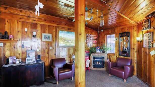 A cozy room with wooden walls, a fireplace, leather chairs, and a large window. - Cedar Village Motel (Spokane)