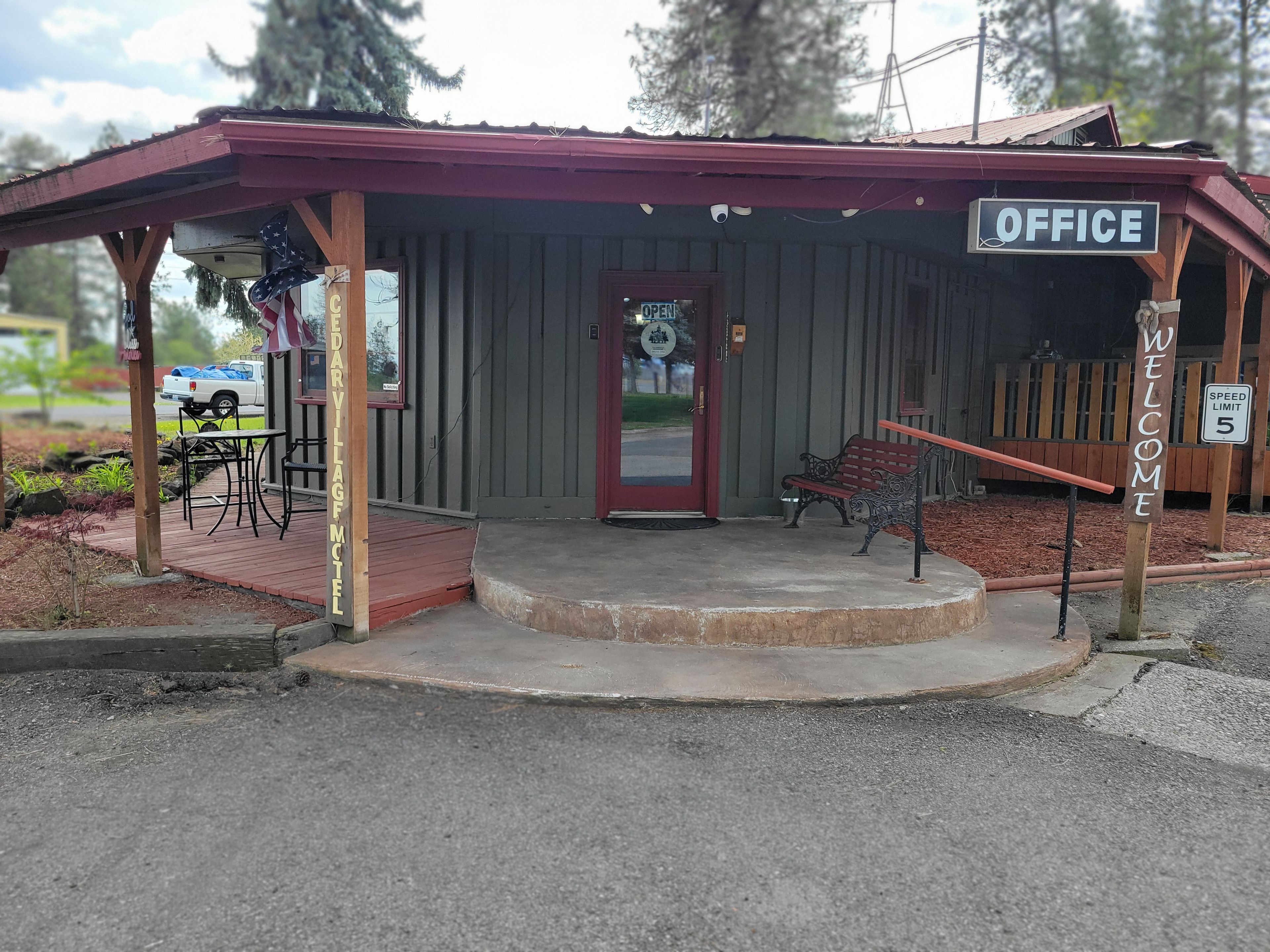 Un edificio pequeño con techo rojo, un cartel que dice 'OFFICE' y un letrero de 'BIENVENIDOS'.
