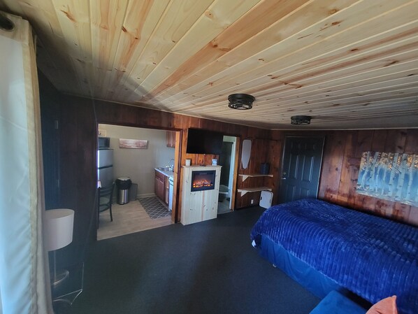 Una habitación con cama, chimenea, zona de cocina y puerta que da a otra habitación.