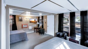 A hotel room with a bed, a desk, a chair, a window with curtains, and a view of the outside. - Cedar Village Motel (Spokane)