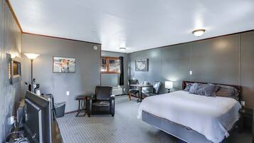 A hotel room with a bed, a desk, a chair, a lamp, and a map on the wall.