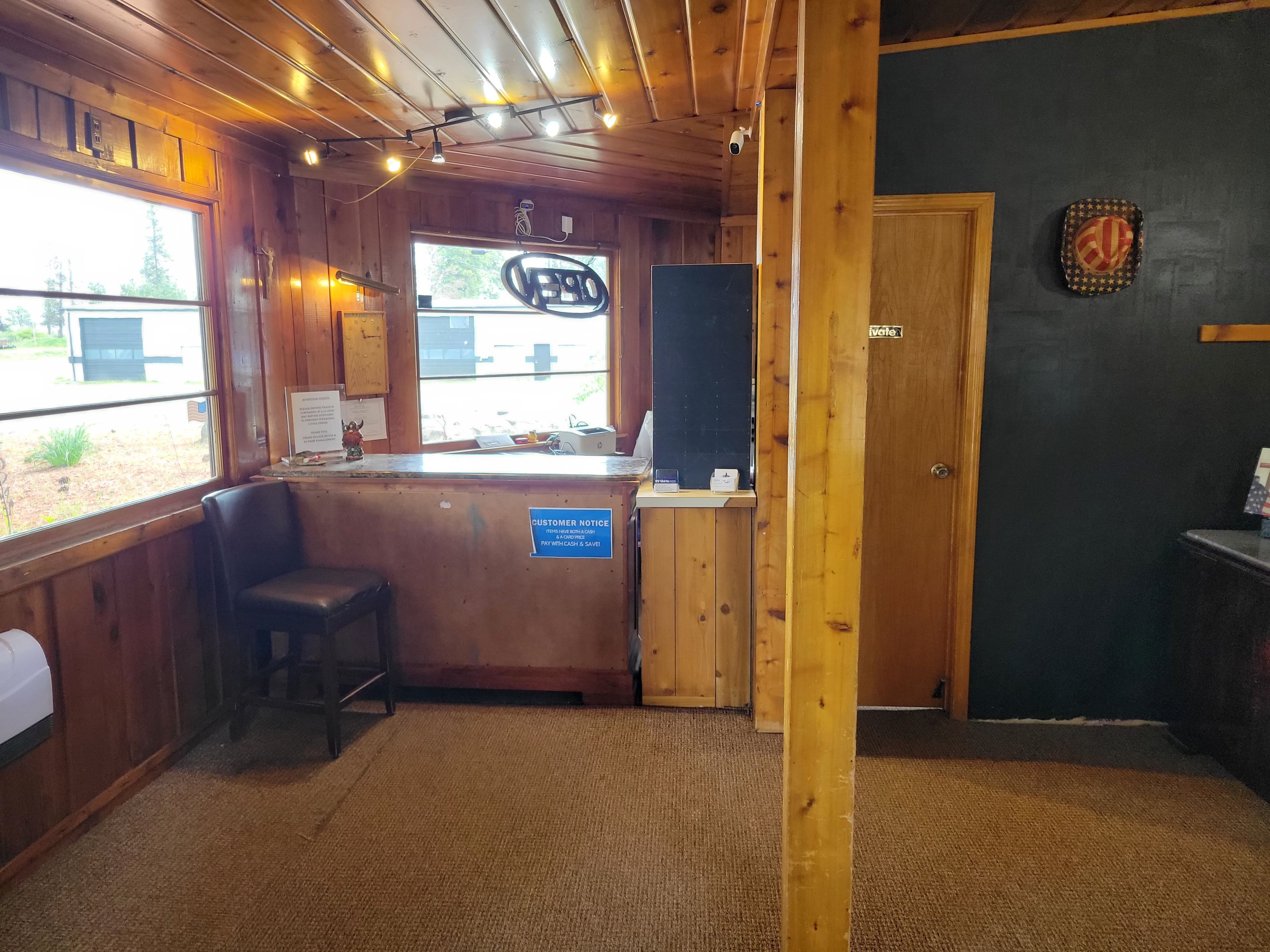 Interior de madera con mostrador de recepción, un cartel que indica las opciones de pago y una vista por la ventana.