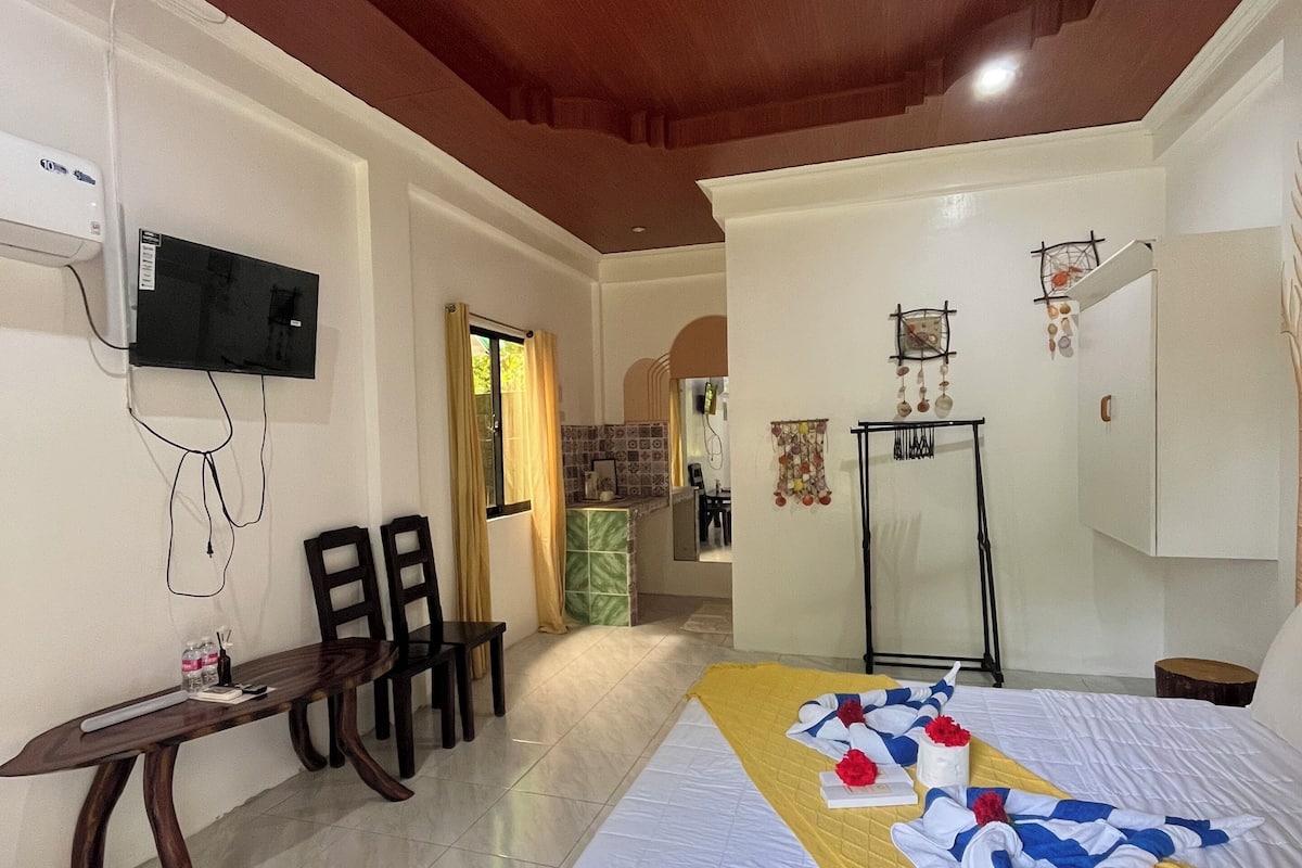 A hotel room with a bed, a desk, chairs, a TV mounted on the wall, and a small table.