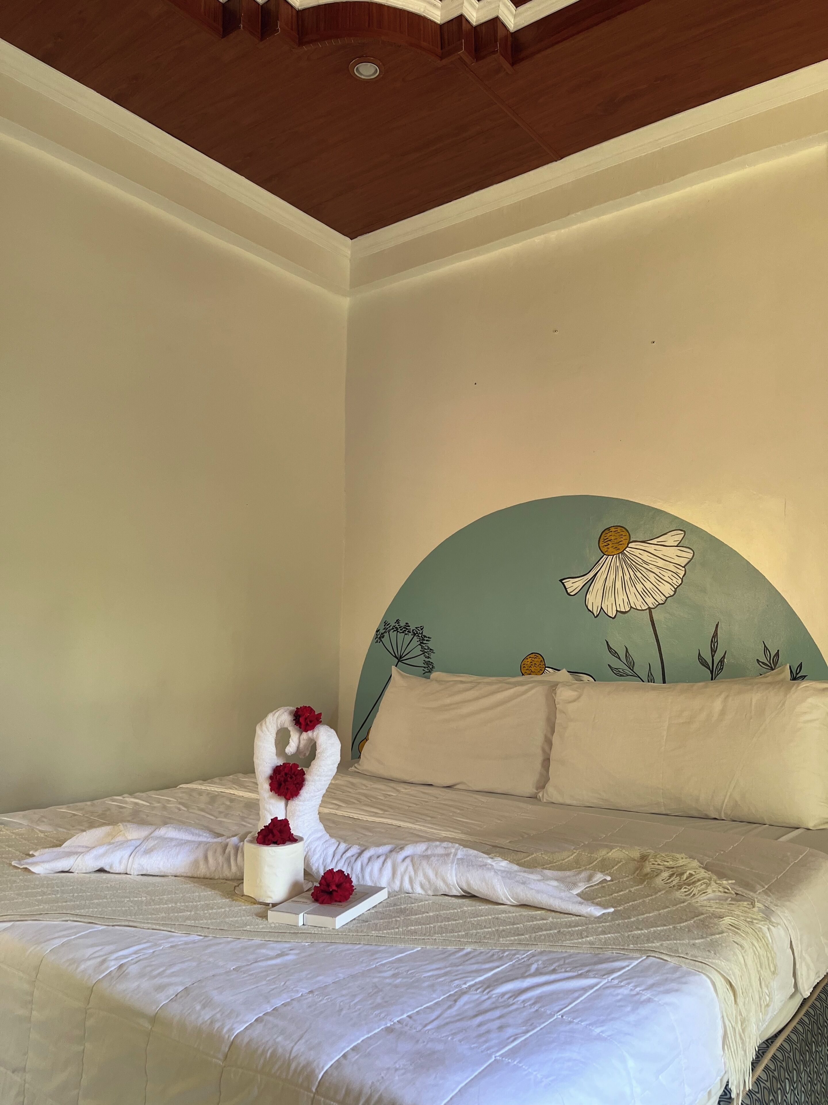 A bedroom with a bed, pillows, a decorative headboard, and a wall with a painted flower design.