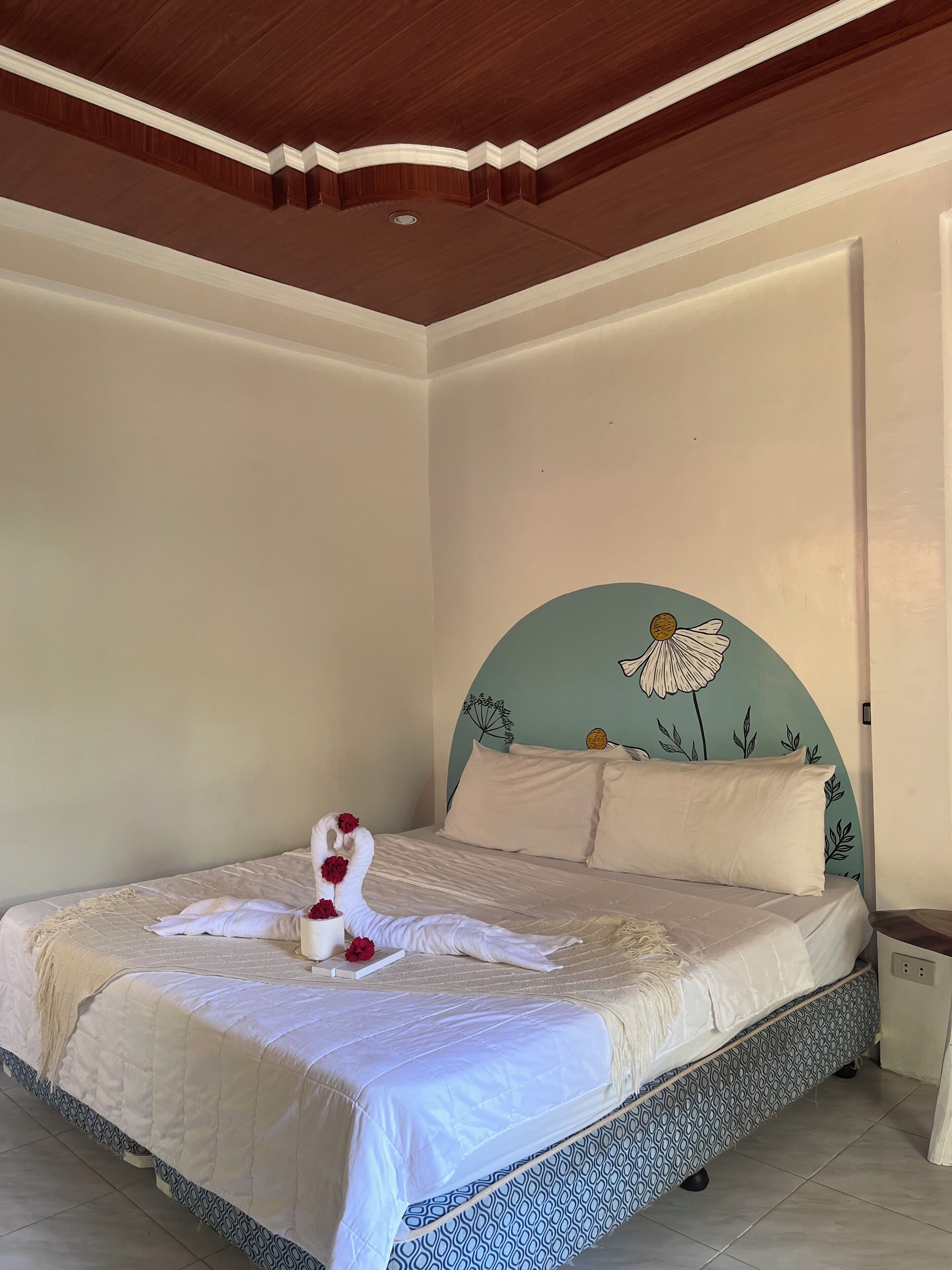 A neatly made bed with a decorative swan and red flowers, a patterned headboard, and a tiled floor.