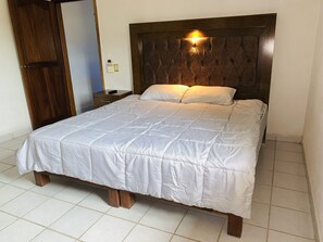 A neatly made bed with a wooden headboard and a white quilt. - Turtle Condo at sun house whit pool (Lomas del Calvario)