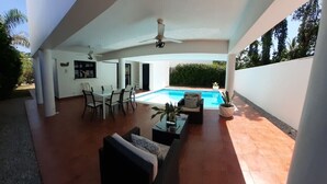 Un espace extérieur avec piscine, doté d’un ventilateur de plafond, de sièges et offrant une vue sur la piscine.